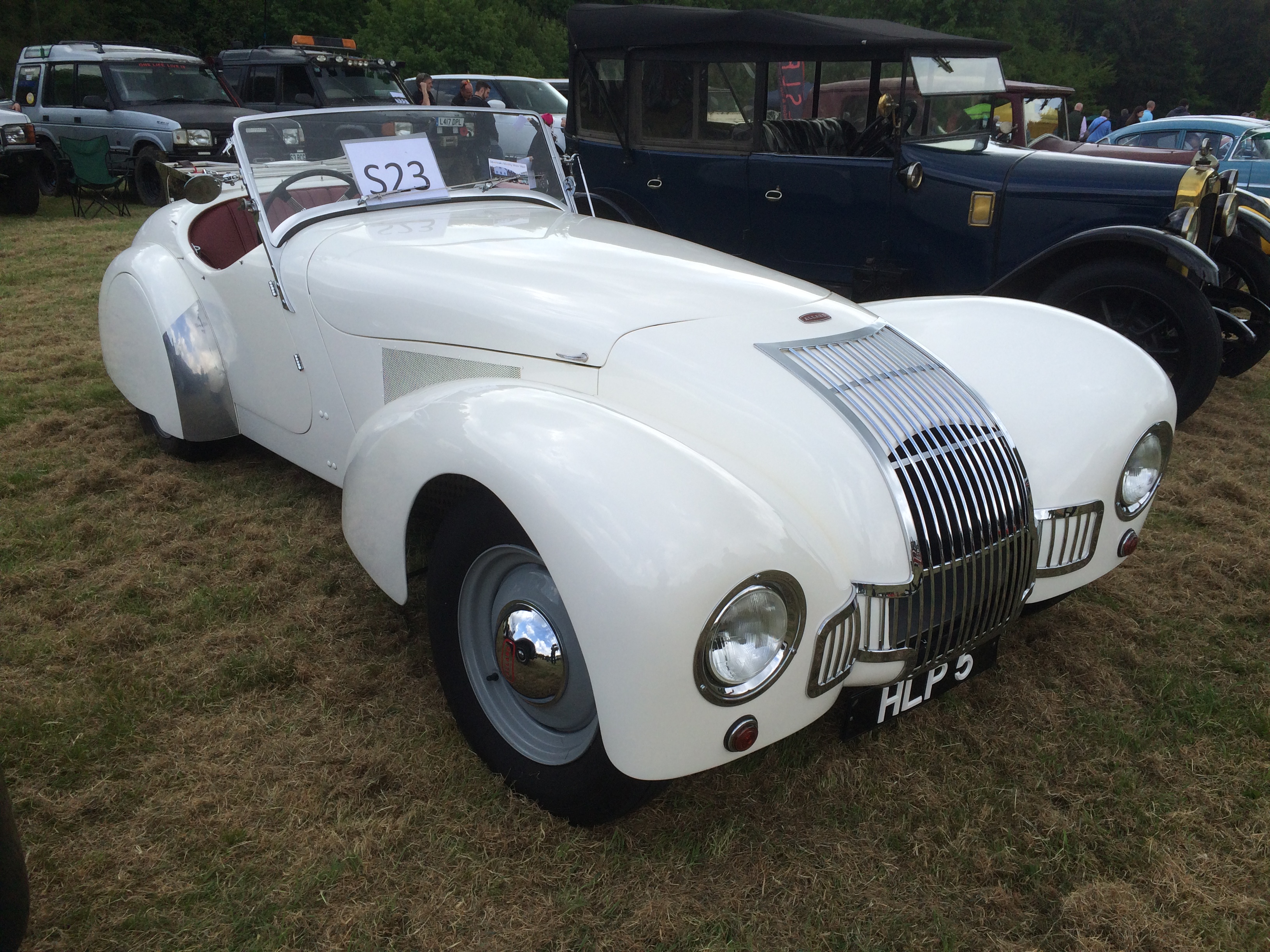 Valence Hillclimb - Page 1 - Events/Meetings/Travel - PistonHeads - The image showcases a classic white car parked on a grassy field. This car is the main focus of the image, with bold white graphics running across its hood. The car seems to be an antique, as suggested by descriptions provided in the previous format. In the background, there are several other vehicles parked, including an old truck. However, these are not as prominent or detailed as the white car in the foreground. The car's placement on the grass and its vintage appearance suggest that it could be on display at a classic car event.