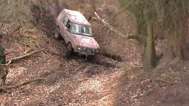 Wilton off road centre pics 11/03/2012 - Page 1 - Off Road - PistonHeads - The image depicts a challenging off-road terrain with a vehicle, likely a jeep, embedded half-way up a steep incline covered in mud and rocks. There are multiple trees along the edge of the road, suggesting the area may be forested. The vehicle appears to be in motion, navigating the rough landscape. The surroundings appear to be like a rural area, possibly in a mountainous region, given the verticality of the terrain.