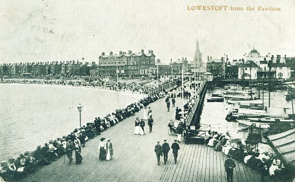 Lowestoft - Page 2 - East Anglia - PistonHeads - The image is a vintage black and white photograph capturing a bustling beachfront promenade known as "Lowestoft from the Pavillion." It shows a crowd of people enjoying the seaside on this day, with the calm body of water that is the sea in the background. The beach is populated with a multitude of people, some walking, some standing, and others relaxing. The photograph provides a glimpse into the past, capturing a moment of leisure and enjoyment by the sea. The age of the photograph and the style of clothing worn by the people indicate it's from an earlier era, likely in the late 19th to early 20th century.