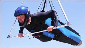 Gliding. - Page 5 - Boats, Planes & Trains - PistonHeads - The image features an individual engaged in a high-flying activity. They are wearing a wetsuit with blue and black colors and are attached to a parachute via a harness. The individual is gripping a metal pole, providing support and control in mid-air. The background is a clear, blue sky, indicating that the scene takes place during the day. The setting seems to be an outdoor adventure scenario, possibly involving water or similar outdoor activities.