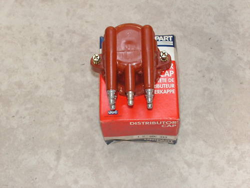 Pistonheads Arm Rotor - The image shows a red safety cap placed on its packaging box. The cap is the easily recognizable orange and black variation, commonly used in construction zones and industrial environments for head protection. The packaging box has a label that reads "distributor CAP," indicating it is intended for sale to retailers or other distributors. There are also definitions and instructions, written in French, which are likely part of the product's labelling requirements. The overall setting is a flat surface, providing a neutral backdrop that contrasts with the prominent red packaging box.