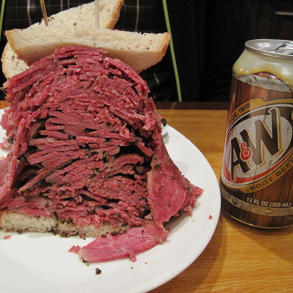 What have you ordered, which turned out substantially bigger - Page 5 - The Lounge - PistonHeads - This image depicts an enormous, open-faced sandwich served on a white plate, which is sitting on a wooden table. The sandwich base appears to be a corned beef, as it has the distinctive reddish shredded texture. It's piled high with slices of rye bread, held together with toothpicks. Above the plate, there's an open can that displays the brand "An" and the text "Rut Beer," suggesting the sandwich may be from a restaurant or event with this beer sponsorship. The can and plate are the main object of focus, with hints of a person in the background, but they are not the primary focus of the image.