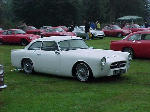 Pistonheads Gilbern Prototype - The image showcases a vibrant gathering of classic cars in a grassy field. The centerpiece is a pristine white Jaguar XK 120, the renowned sports car, which seems to be the star of this vintage automobile event. The car has a gleaming white body and black soft-top roof, a classic style that is reminiscent of the 1950s. Around it, there is a sea of classic cars, painted in a palette of red and white, suggesting that this gathering might be a themed event or a classic car show. The field is lush and green, providing a contrasting backdrop to the shimmering cars. In the background, amidst the vintage revelry, a few people can be seen, perhaps car enthusiasts or attendees of this classic car meet.