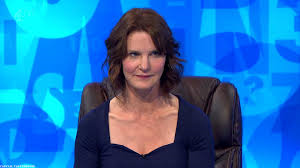 Weird Secret crush's from TV  - Page 20 - TV, Film & Radio - PistonHeads - The image is a photograph of a woman seated in a chair against a blue background that has various shapes and letters on it. She has short brown hair and is looking directly at the camera with a neutral expression. The woman is wearing a dark blue V-neck top. The style of the image suggests it might be from a television show or a game show, given the setting and the presence of the woman who seems to be a host or presenter.