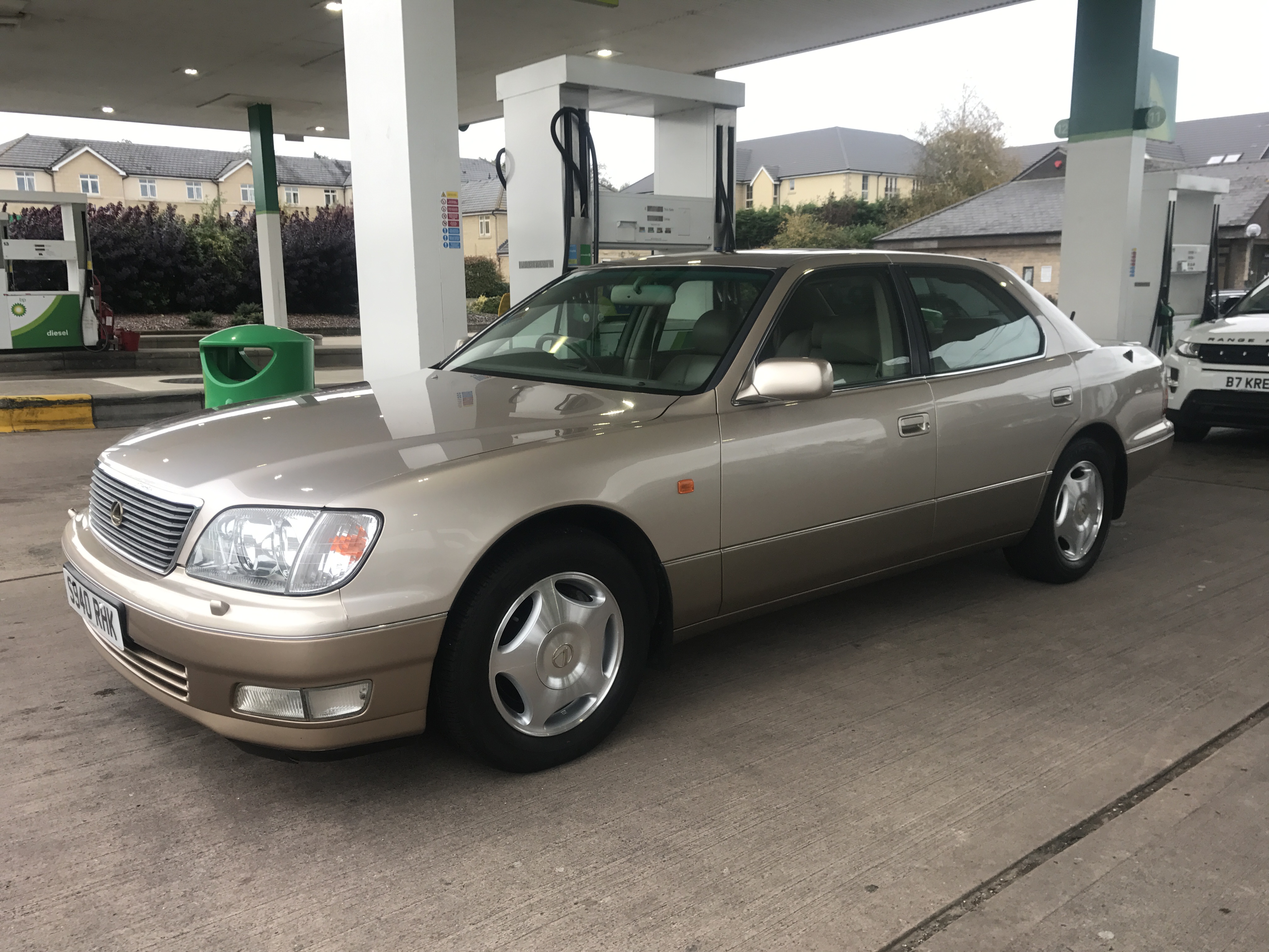 Best smoker barges 1-5 large [vol11] - Page 499 - General Gassing - PistonHeads - The image depicts a beige-colored sedan parked at a gas station, with a green canopy visible in the background. The car features alloy wheels and has a European-style license plate. There is a pump and the gas station's logo in the vicinity, suggesting the proximity of facilities. The background is a bit blurred, indicating a focus on the car. The lighting appears to be natural, potentially indicating a clear day.