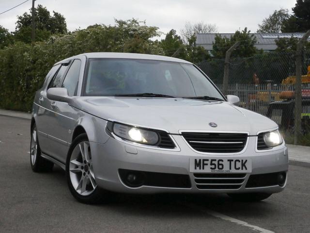 95 year differences - Page 1 - Saab - PistonHeads - The image showcases a silver compact car with a license plate reading "MF56 TCX." The vehicle is in motion, traveling down a street. The surrounding area includes a fenced area, some vegetation in the background, and a building partially visible to the right. The setting appears to be during the day under an overcast sky.