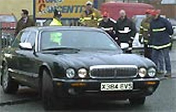 Yellow vests - fuel protest day of action in France  - Page 75 - News, Politics & Economics - PistonHeads - The image depicts an outdoor scene where a black car is being towed by a truck. Several people are present, some near the truck and others standing around the car, suggesting that they may be involved in a recovery or investigation process. There's also an object resembling a fire hydrant in the vicinity of the car. The setting appears to be a road or street, as indicated by the presence of the tow truck and people gathered around the vehicles.