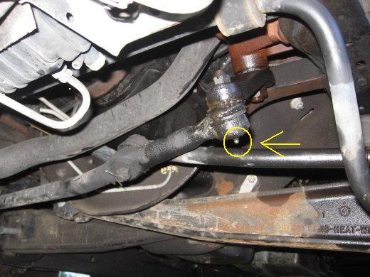 Noise Steering Pistonheads - The image focuses on a suspension mount on a vehicle. It's taken from an angle that provides a clear view of the mechanical component. This component is connected to other parts of the vehicle's structure, which includes a metal frame and possibly a suspension coil. There's a close-up of a hole, possibly indicating a loose or damaged part that needs addressing. Additionally, a yellow arrow draws attention to the hole, suggesting it's an issue that requires attention or repair.