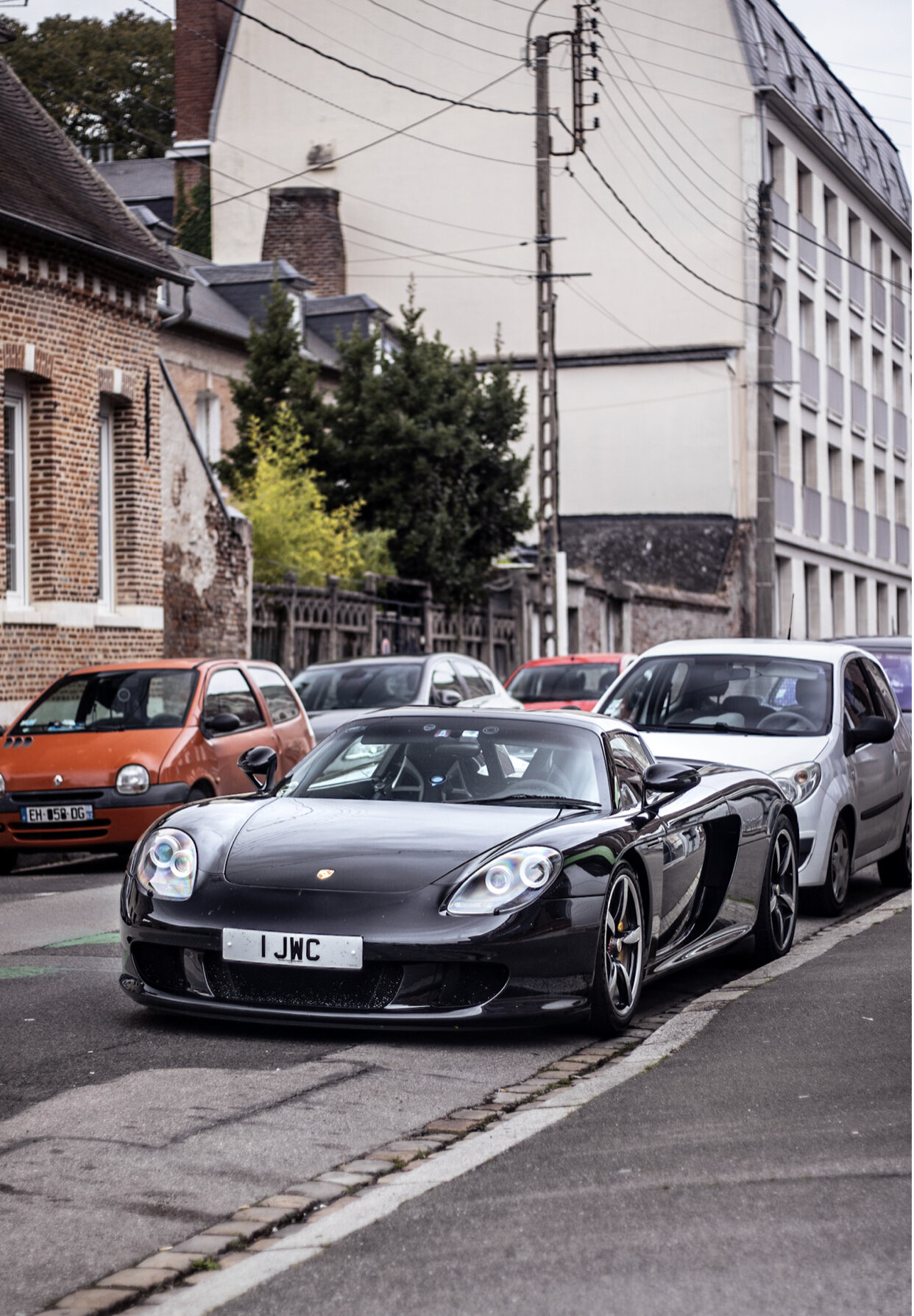 Show off your GT, past and present... - Page 67 - 911/Carrera GT - PistonHeads UK - The image features a dynamic street scene with a focus on a black sports car parked alongside the road. The car has distinctive racing stripes and is prominently displayed in the frame, suggesting it might be the main subject of the photo. It's positioned between two cars, one red and the other white, indicating a busy urban area. In the background, there are buildings with signs, trees, and a clear sky, adding to the overall atmosphere of the cityscape.