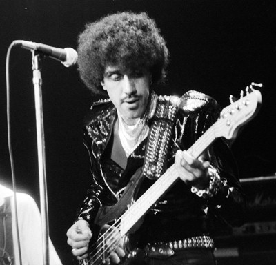 Pistonheads Swansong Albums - This is an iconic black and white photograph of a musician performing on stage. The individual is holding a guitar and is dressed in a black, studded outfit that accentuates a sense of movement and energy. The man appears focused and highly engaged in his performance, embodying the intensity of the scene. The image captures a moment of live music, conveying the atmosphere and the musician's dedication to the craft.