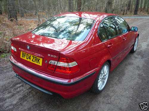 Godbye Volvo, Hello BMW! - Page 1 - East Anglia - PistonHeads - The image depicts a close-up view of the rear of a red BMW car parked on a dirt road. The car features a sleek design with tinted windows, dual exhaust pipes, and a license plate with the letters "B04 ZRK". The setting implies a tranquil, wooded area, indicating that the car might be on a remote excursion or in a forested location. The environment suggests an outdoor adventure or exploration, possibly a road trip or hiking excursion.