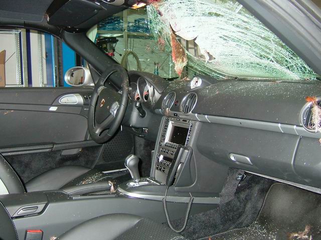 Pistonheads - The image shows the interior of a car with apparent damage from a broken window or another form of impact. The front side window is shattered, allowing visibility through the webbing of the shattered glass. Several objects are scattered around the interior, adding disarray to the scene. The steering wheel is on one side, with the speedometer and the car's controls visible next to it. The interior upholstery is black, which contrasts with the brighter interior lighting. There are no people visible in the photograph.