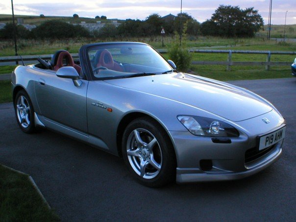 My Car - Page 1 - Readers' Cars - PistonHeads - The image shows a silver Honda convertible parked on the side of a road in a rural area. The car has a sleek design with a visible convertible top and a sunroof. It's an overcast day, and the serene landscape features expansive fields and a clear sky. The car's license plate is visible, and a blue car is parked behind it. The overall scene conveys a sense of peacefulness and tranquility.