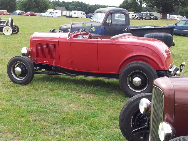 NSRA Hot Rod Supernats - Page 1 - Yank Motors - PistonHeads - The image depicts a picturesque scene of vintage cars parked on a lush green field. The cars, including a striking red antique with a convertible top, are the focal point of the image. The field is dotted with tents, indicating that this could be a car show or a similar event. The atmosphere is nostalgic and serene, with the green of the field contrasting beautifully with the various colors of the cars, making for a visually appealing image.