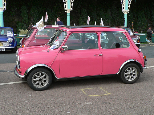 what colour? - Page 1 - Classic Minis - PistonHeads - This image captures a vibrant scene on a street where a row of colorful vintage cars is parked. The most prominent car is a small, bright pink, almost reminiscent of a certain "Muppet" car. It is positioned right next to a blue car, creating a contrast of colors. All the cars are stationary, parked at the side of the street, and appear to be from an older model, adding a touch of nostalgia to the scene. In the background, there's a glimpse of a building and what seems to be some greenery, which adds context to the location. The image exudes an aura of a casual day out, with these vintage cars on display.