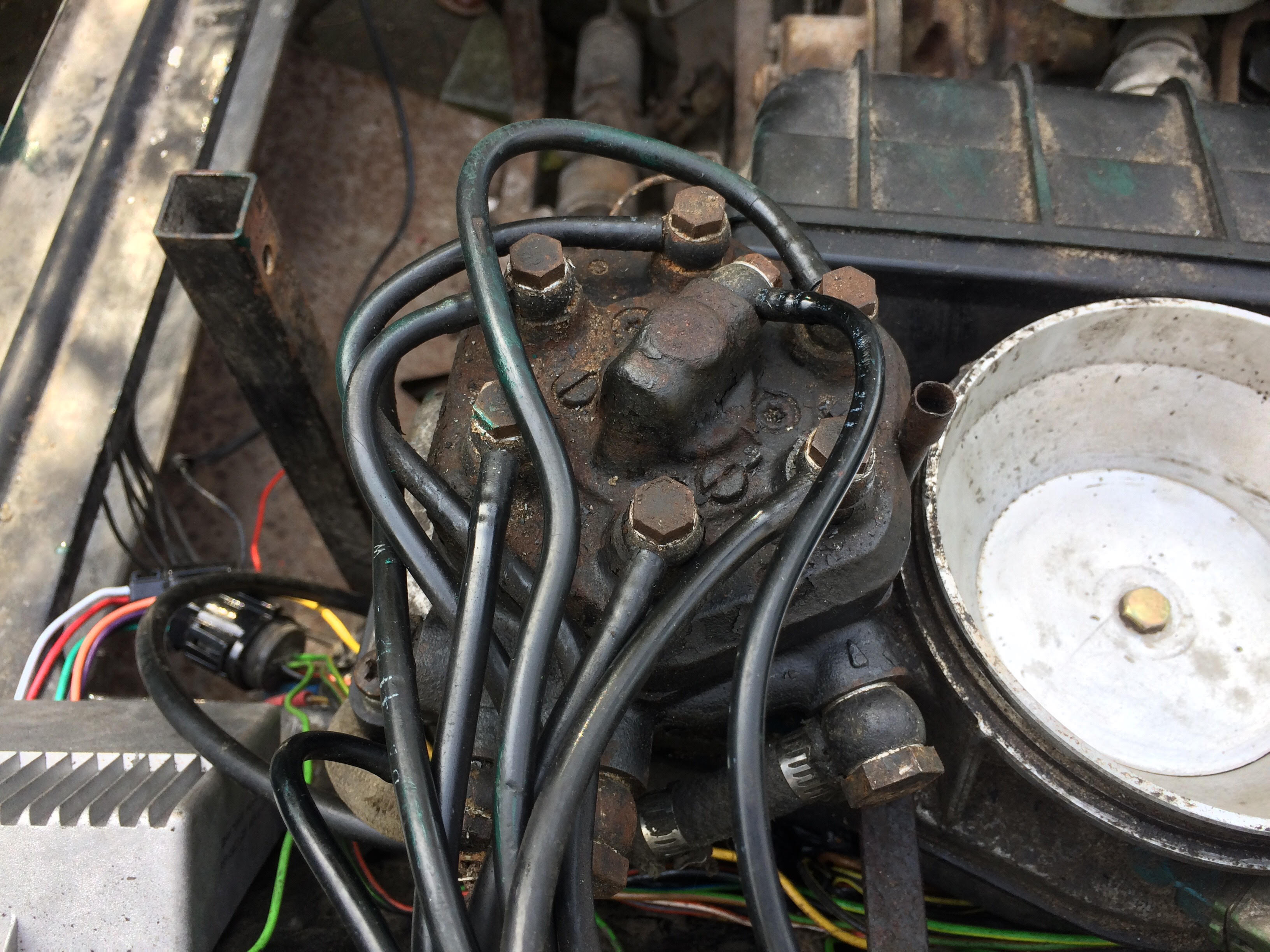 None starter - Page 1 - Wedges - PistonHeads - The image shows the underneath side of an engine or machine. There is a complex tangle of various electrical and mechanical components, including a prominent black object, possibly a pump or engine component, surrounded by an array of wirings and tubes that are tightly packed together. The background appears to be a garage or repair facility. The colors are a combination of black, brown, and green, and the image has an algorithmic texture, possibly due to a camera effect or digital rendering. The scene presents a sense of complexity and technical precision indicative of a mechanical repair or assembly process.