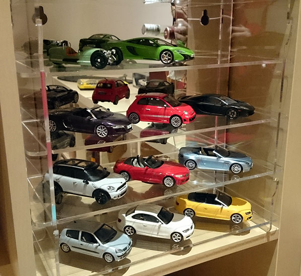 Repainting 1:43 Models? - Page 1 - Scale Models - PistonHeads - The image showcases a vibrant display of toy cars in a transparent case. There are at least 10 cars in various colors, including green, red, black, silver, blue, and gold. The cars are arranged on multiple shelves, and some are even displayed in three dimensions due to the glass doors of the case. The variety of colors and types of toy cars enhances the appeal of the display, likely designed to attract the attention of children or collectors.