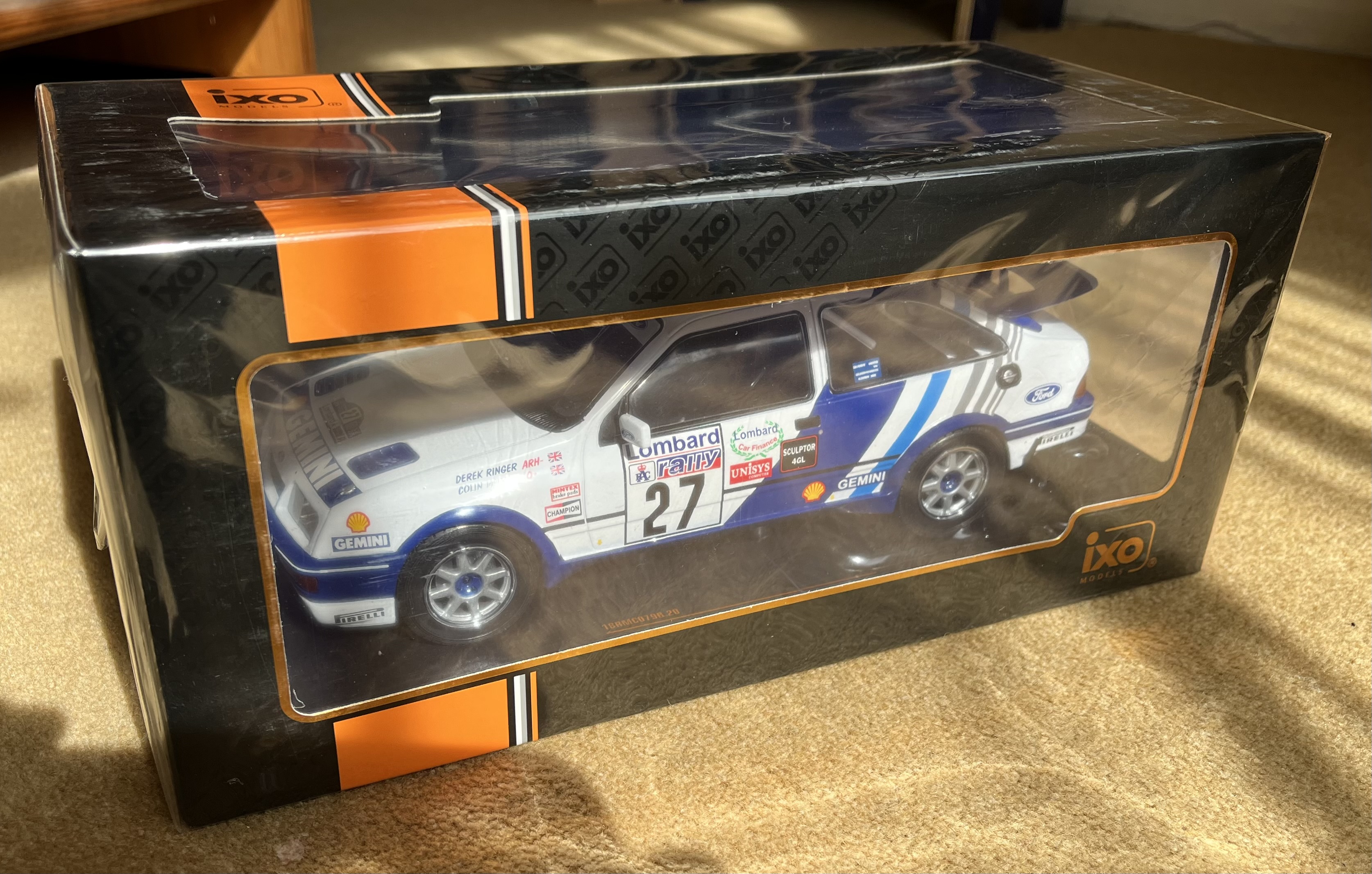 Pistonheads - The image shows a boxed toy car placed on a surface. The packaging is predominantly black and orange, with the toy car displayed in the front. It appears to be an exotic sports car, possibly a model of a racing car given its design and detailing. On the side of the packaging, there's a logo and some text that are not clearly legible due to the angle and resolution of the photo. The toy car has a realistic appearance with detailed graphics and features like wheels and headlights. There's a slight reflection on the surface beneath the box, indicating it might be made of glass or another reflective material.