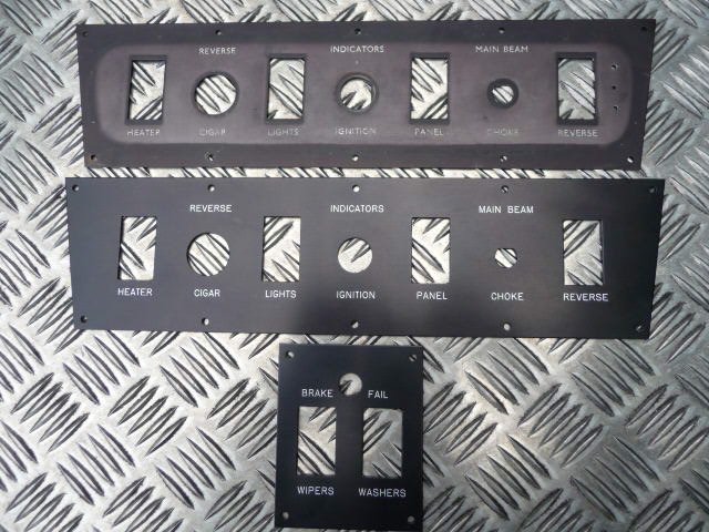 Dashboard panel images - Page 1 - Classics - PistonHeads - The image shows two black panels with multiple control buttons, likely intended for a vehicle's dashboard. The panels are arranged on a textured metal surface that could be part of a workbench or shop floor. Each panel comes with a reversible orientation of buttons, suggesting that they can be flipped to indicate whether lights, brakes, ignition status, and other vehicle functions are on or off. One panel has "REVERSE" and "FAIL" labels on it, indicating specific controls, while the other is depicted in a partially extended state to demonstrate the reversible set. The overall setting is industrial and functional, emphasizing the purpose of these controls in a vehicle's settings.