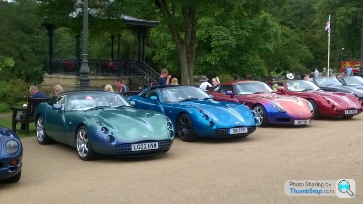 "Thrills in the Hills" Peak District TVR run Sat May 21st - Page 1 - TVR Events & Meetings - PistonHeads - The image shows a scenic outdoor event focused on vintage sports cars. Several classic and unique designs, varying in color and model year, are neatly lined up on a paved area, commanding attention and admiration. Behind these beautifully crafted machines, a row of spectators is gathered, some standing and others sitting on a bench, all seemingly enjoying the rare display of these iconic vehicles. The backdrop of the event is a lush park with verdant trees, indicating a pleasant day for the auto enthusiasts.