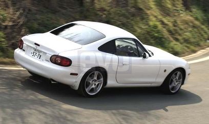 Tonneau cover fitted & a hard top?? - Page 1 - Mazda MX5/Eunos/Miata - PistonHeads - The image features a white two-door coupe, driving on a road that curves to the right. The car's design and the windows are reflecting the curvy road and the surrounding environment, indicating movement. The car has red taillights and wheels, and the license plate reads "5Z87". The setting appears to be a green and leafy hillside with trees visible in the background.