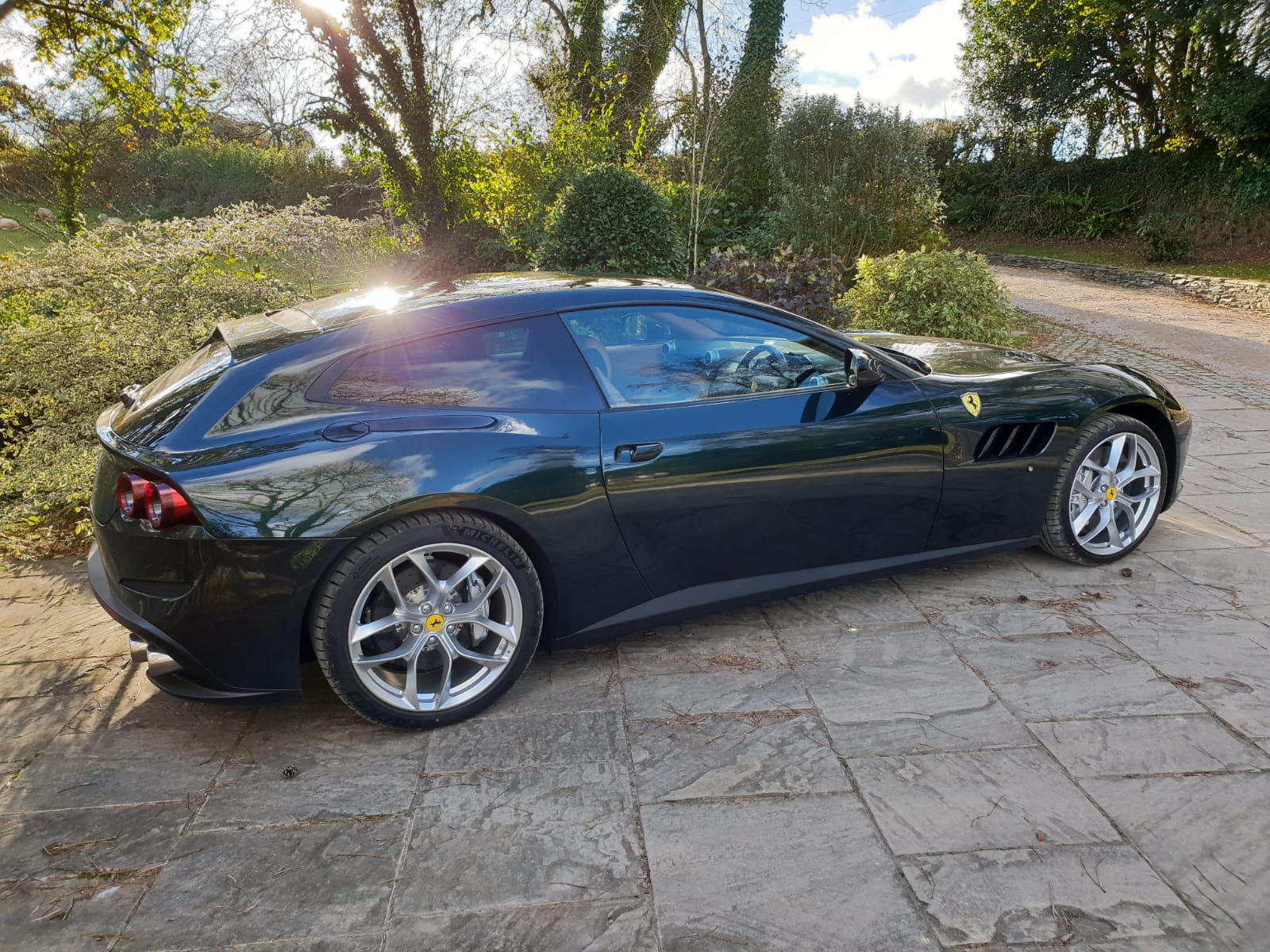 RE: New Aston Vanquish Zagato Shooting Brake images - Page 3 - General Gassing - PistonHeads - This image features a dark green Ferrari sports car parked on what appears to be a cobblestone driveway. The car has a sleek design typical of high-end sports cars, with a distinctive front grille and the iconic emblem on the side. It's equipped with large, alloy wheels, which suggests it might be a performance or race variant of the model. The setting is outdoors during the daytime, as indicated by the natural light and shadows cast on the ground. There are no visible texts or distinctive branding in the image beyond the Ferrari logo.