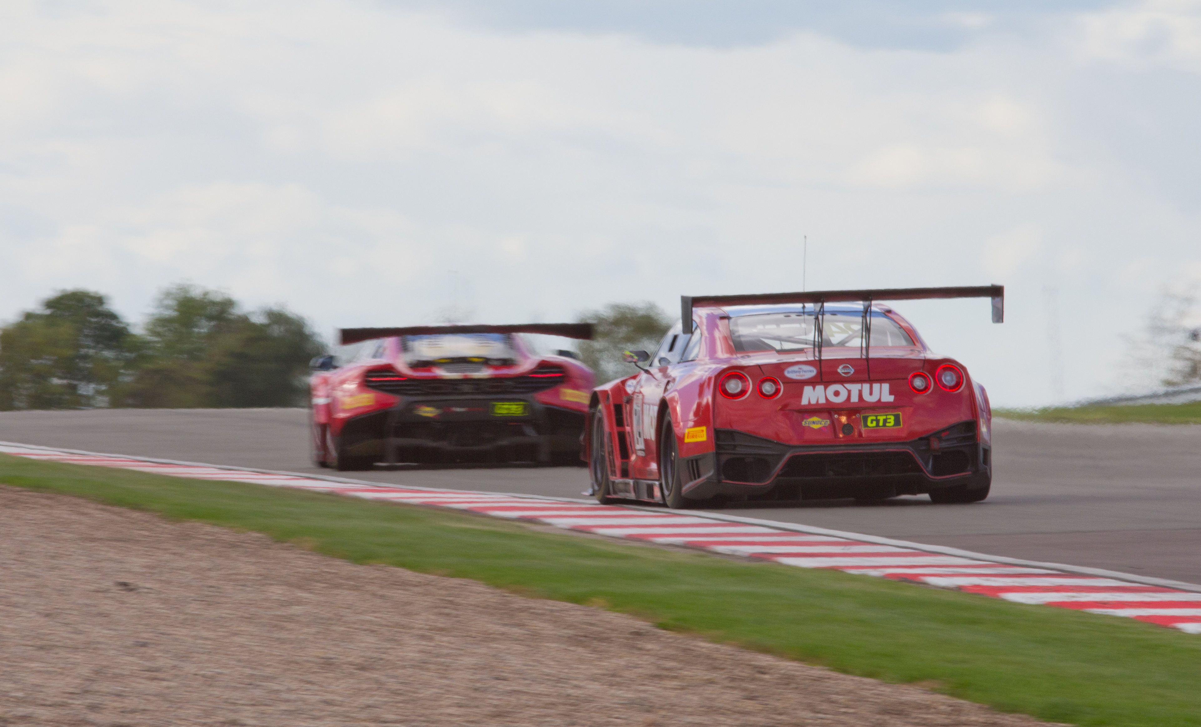 Random Photos : Part 5 - Page 7 - Photography & Video - PistonHeads UK - The image is a dynamic photograph capturing the intensity of an automobile race. In the foreground, two race cars with prominent sponsor logos are in close proximity, appearing as if they are competing for the lead. One car is driving closely behind the other, demonstrating the aggressive nature of the sport.

The background features a long straight stretch of racetrack that curves gently to the left, lined by barriers and safety fencing. The setting is during the day under clear skies with ample sunlight casting shadows on the track. There are no visible spectators in the stands or around the track, suggesting either an early stage of the race or a less populated event.

The cars' liveries include the manufacturer's logo and additional sponsor decals, which are common features in professional racing to promote their partners. The overall composition of the image conveys motion and competition, with the focus on the vehicles and the racetrack environment.