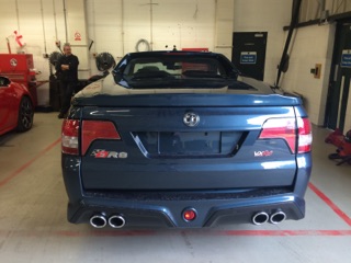 A car is parked on the side of the road - Pistonheads - The image depicts a scene inside a garage or service station, where there is a focus on a blue sedan parked on a red and white striped service area. The car's rear end is clearly visible, showcasing its taillights, bumper, and hints of exhaust pipes. There's a logo visible on the center of the trunk, indicating it's a Hyundai vehicle. 

A man is present in the background, possibly an employee or a patron engrossed in maintenance or inspection of the car. The garage has a variety of equipment around, suggesting it is a well-used facility for car care. The ambient lighting and the closed nature of the doors indicate it might be a professional workshop rather than a private garage.