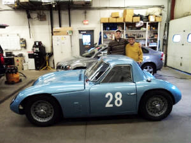 Early TVR Pictures - Page 34 - Classics - PistonHeads - The image showcases a vintage blue car in a garage setting. With two men standing by, the car's number 28 is prominently displayed, suggesting it could be a race or rally vehicle. The garage is well-organized, with shelves stocked with various items, reflecting a place where automotive repair and maintenance occurs.