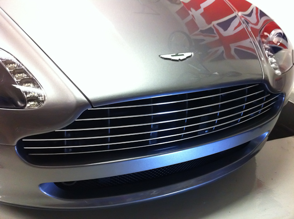 Vantage grille design: 6-bar vs. 8-bar - Poll. - Page 1 - Aston Martin - PistonHeads - The image showcases the front end of a silver car. The car features an interesting design element, a Union Jack symbol representing the UK, which is integrated into the grille. The car has a sleek chrome bumper and the body of the car has a shine, reflecting the manufacturer's high-end finishes. The design is contemporary and sophisticated, indicative of a luxury car model. The Union Jack symbol suggests that the car may be produced by a British company or manufactured in the UK.