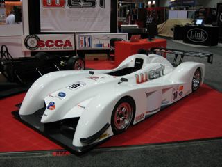 Pistonheads - The image features a white race car on display at a trade show. The car is positioned on a red floor mat, giving it a striking contrast. On a red carpet, the car is parked behind a small orange sign. In the background, a display banner with the letters "WEL" and the acronym "SCCA" can be seen, suggesting that the exhibition is related to racing or automotive. Despite the focus on the single car, the presence of several other display items in the background indicates a bustling trade show environment.