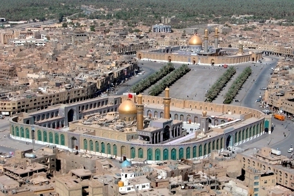 Mosque Building - The image presents an overhead view of the Grand Mosque of Qaraichi, also known as the The Protoplast of Islam's Role in its Surroundings ' Gallery of Calligraphy, in Karachi, Pakistan. The distinctive architectural features of the mosque are prominently displayed, including its large golden dome and, in the foreground, the green roofed buildings that serve as facilities like schools and a hospital. Surrounding the mosque is a bustling cityscape with numerous buildings and a few vehicles visible on the streets. The image provides a sense of the mosque's location within the urban environment.