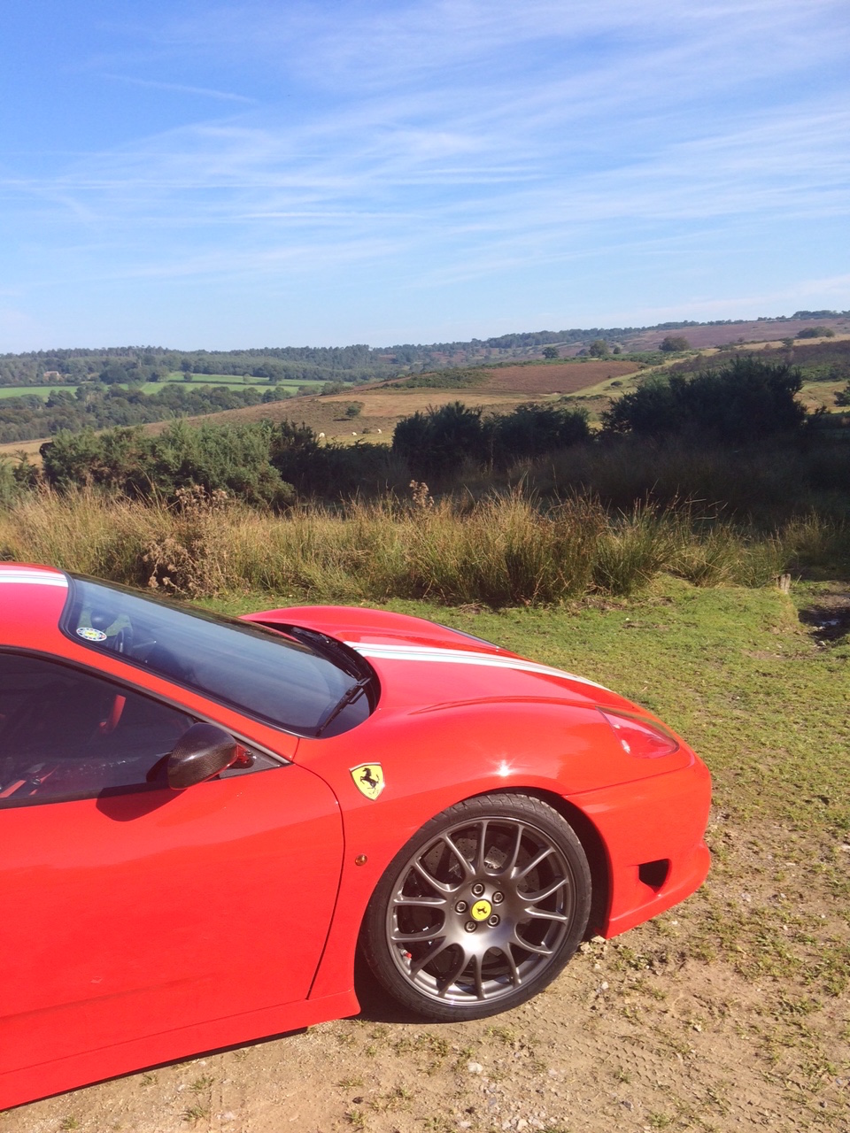 What did you do with your Challenge Stradale today? - Page 1 - Ferrari Classics - PistonHeads - The image showcases a vibrant red Ferrari sports car parked on a grassy area under a clear blue sky. The car features a sleek, aerodynamic design along with a distinctive Ferrari emblem on the side. The setting appears to be in a rural or countryside location, with fields visible in the background. The overall scene conveys a sense of luxury and the enjoyment of driving through scenic landscapes.