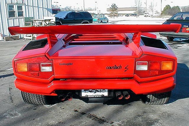 Countach  - Page 9 - Lamborghini Classics - PistonHeads - The image showcases a vibrant red sports car, parked outdoors on a driveway. It's a sleek and stylish vehicle, characterized by its long hood and short tail. The car's design features a prominent rear wing, adding to its aerodynamic appeal. The color matches the hood of the car, with the body in a glossy, putty red hue.