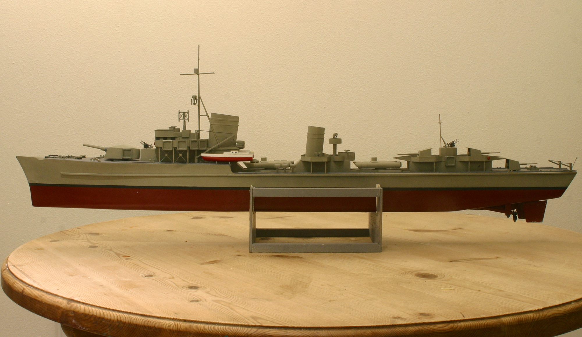 Pics of your models, please! - Page 125 - Scale Models - PistonHeads - The image shows a detailed model ship, painted primarily in shades of gray on a wooden white base. The ship is a battleship with a prominent red stripe. The model is placed on a wooden table with several distinctive features, including a bridge, a stern, and several towers. The model ship is detailed in design, showcasing the intricate structures typical of historical naval vessels.