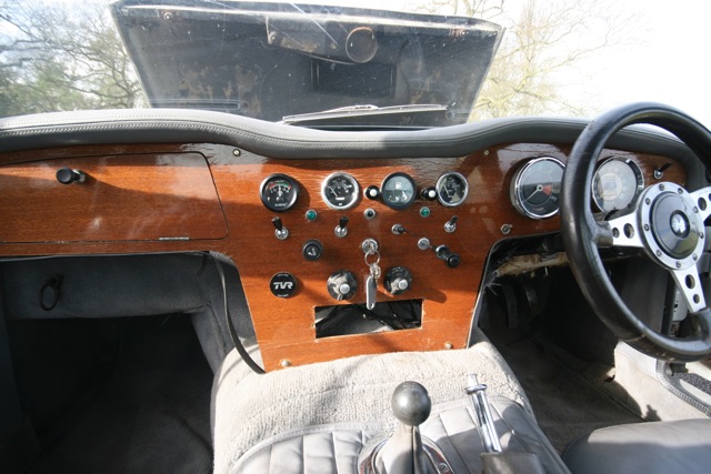 Early TVR Pictures - Page 35 - Classics - PistonHeads - The image shows the interior of a car, focusing on the driver's side. The dashboard is made of wood, with a large cluster of gauges and controls positioned in front of the driver. These gauges include a gas gauge in the center. To the right, there is a traditional steering wheel and speedometer. The car appears to be vintage, given the design and material of the dashboard. There is also a passenger-side door, which is visible in the image.