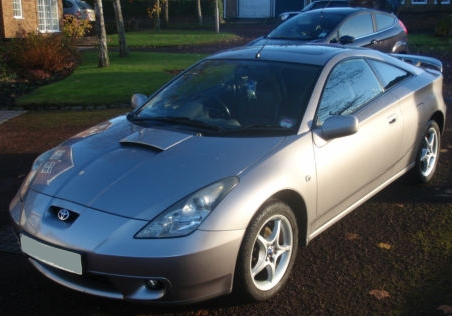 Celica 2001 VVTi-190... Rear bearing fault, advice please... - Page 1 - Jap Chat - PistonHeads - This image features a meticulously well-kept, sleek silver coupe positioned on a gravel driveway. Its design is contemporary with a large rear spoiler and a distinctive air intake area. The presence of a plate number indicates it's a legal roadcar. In the background, there are several other vehicles parked on what appears to be a landscaped residential area. The sun is out, casting a warm glow over the vehicle and the scene.