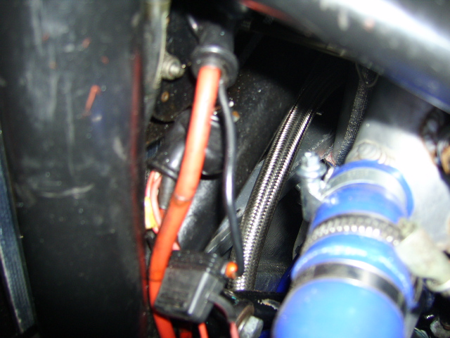 Intermittant Chuggachugga Pistonheads Clubsport Fault - This image shows a close-up view of the inside of an automobile, focusing on the engine area. The most prominent features are the red and black wires, which appear to be car ignition wires, leading towards a battery terminal. These wires are tightly bundled together and have a black connector attached. In the background, there is a glimpse of the blue and silver part of the engine, indicating the presence of some form of metal piping. The overall scene provides a glimpse into the mechanical and electrical components that are used to power a vehicle. The image is a bit blurry and the lighting inside the engine compartment is limited, casting shadows and not allowing for clear detail.