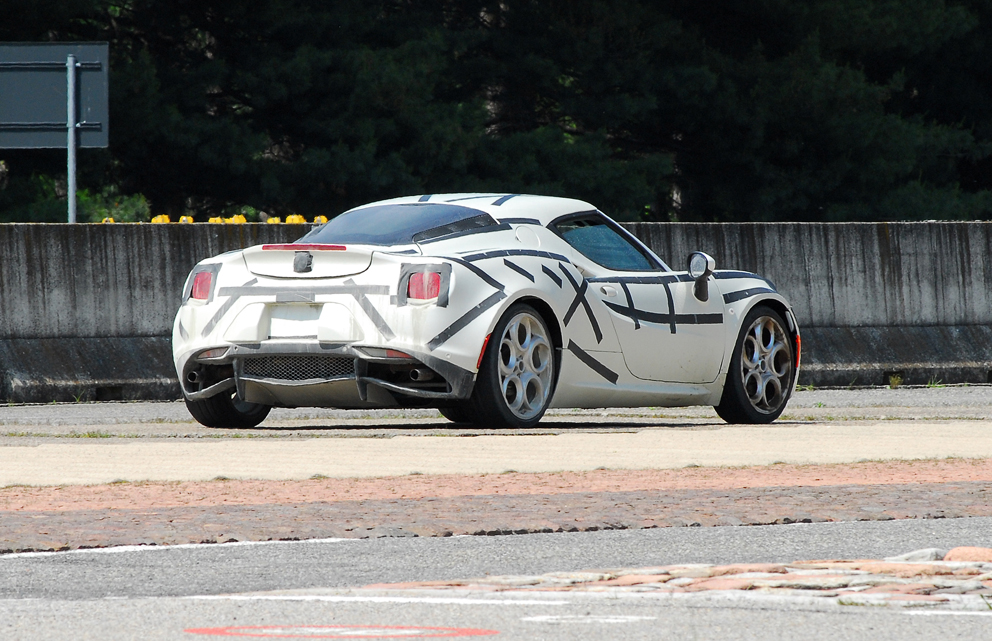 Anyone have any 'inside' info on the Alfa 4C? - Page 12 - Alfa Romeo, Fiat & Lancia - PistonHeads - In the image, a black and white Porsche is parked on the side of a street. The car stands out against the urban backdrop, featuring striking racing stripes. The setting is predominantly green, suggesting trees or shrubs in the background, with a partial view of a street sign and a concrete barrier. The Porsche is positioned near a grassy area, adding a touch of nature to the urban scene.