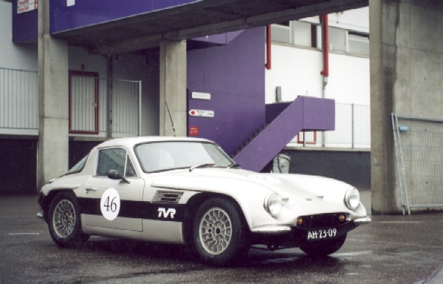 Early TVR Pictures - Page 81 - Classics - PistonHeads - The image shows a white sports car parked under an overhang, with a red brick structure nearby. The license plate of the car is visible and reads "4VL". Adjacent to the vehicle are some steps leading to an entrance. The car's surrounds and design suggest it is of European manufacture. The lighting and color scheme give the scene an aged appearance.