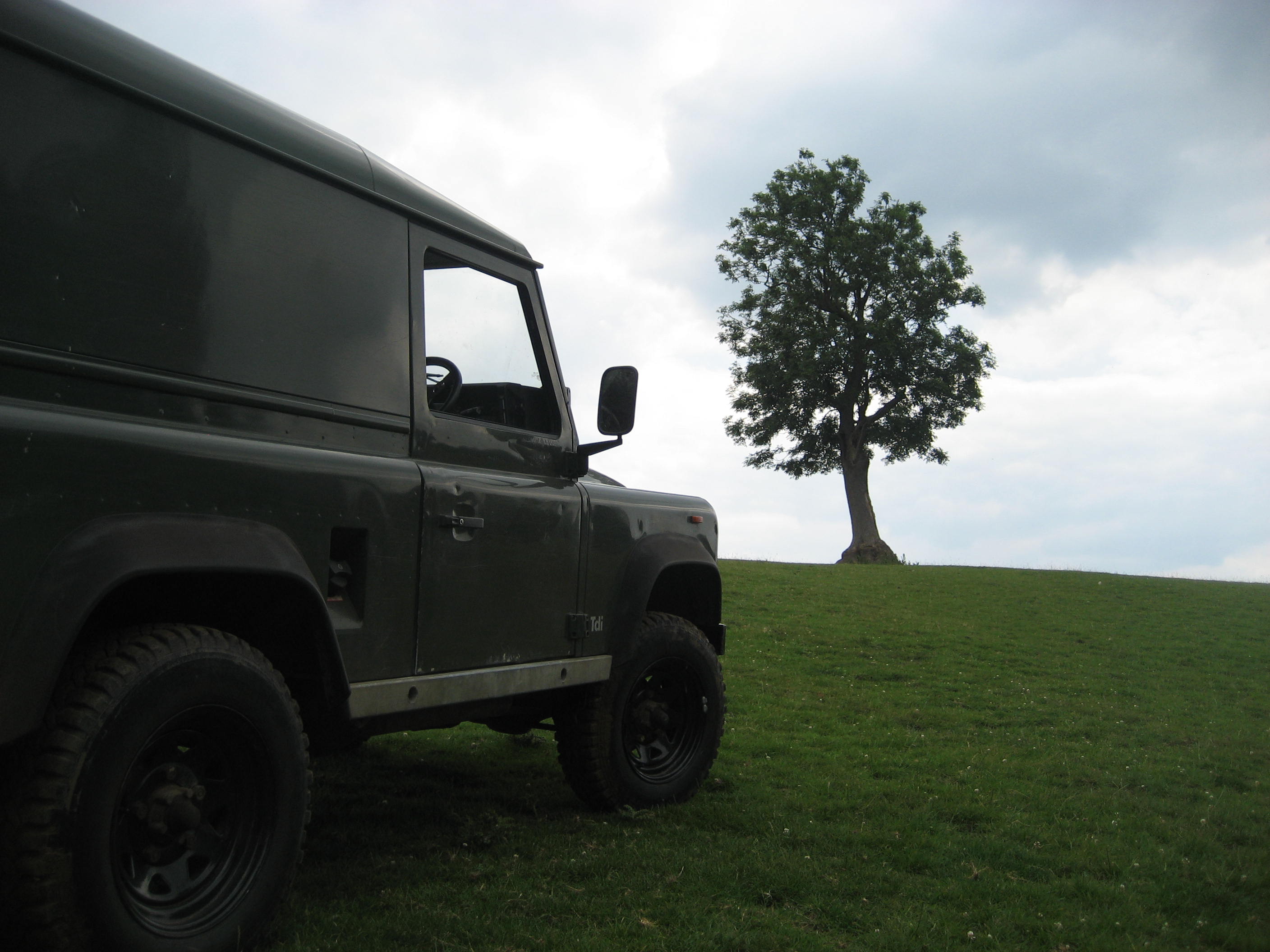 Favourite car pic you took - Page 10 - General Gassing - PistonHeads - The image showcases a rugged green jeep parked on a grassy hillside. The sky above is filled with clouds, casting a soft light over the scene. In the background, a solitary tree stands, adding a touch of nature to the image. The sky, graced by a few scattered clouds, takes up the majority of the scene, creating a contrast with the grounded vehicles and plants. The entire scene has a peaceful vibe to it.