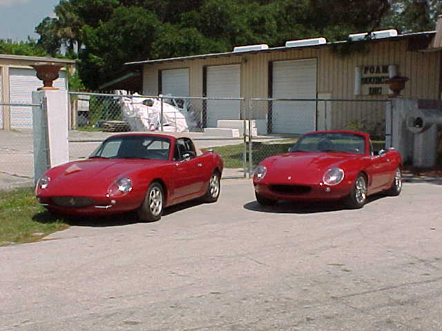 MX5 250GTO body conversion kit - Page 4 - Kit Cars - PistonHeads - The image features two vintage red convertible cars parked on a gravel surface next to each other. They have chrome accents and are positioned on the driver's side. The cars are situated in front of a light beige house, which also has a brick wall and a fence. There's a notable earnestness to the vehicles, suggesting they might be restored or valued models. The overall scene conveys a sense of nostalgia and admiration for classic automobiles.