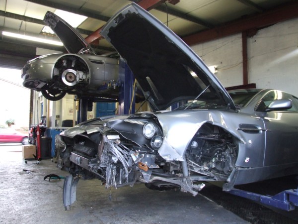 Undressed Dont Squeamish Pistonheads - This image showcases a well-equipped garage where two cars are being attended to. The interior of one car is prominently visible, revealing its open hood and various parts scattered about inside the car. The other car is also being worked on, with its side slightly lifted up. The environment is well-lit, indicating its status as a professional garage, possibly for auto parts or mechanic services. The mechanic's tools, such as a spoke wrench and a cup, are also visible, reinforcing the atmosphere of active work.