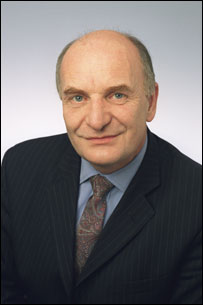 Pistonheads - The image is a headshot of a man, presumably taken for professional purposes such as a company website or a business directory. He is wearing a dark suit with a light blue shirt and a dark tie. The man has short, graying hair, and he appears to be middle-aged. He is looking directly at the camera, and his expression is neutral. The background is plain and does not draw attention away from the subject. The photograph is well-lit, highlighting the individual's features.