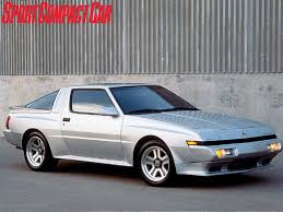 starion buyers guide - Page 1 - Jap Chat - PistonHeads - The image features a sleek, metallic coupe prominently positioned in the center of the frame. The car is parked against a wall with a silver, corrugated finish. The vehicle appears to be an older model sports car, characterized by the 4-door design. A text overlay, positioned above the car, reads "SPORT COMPACT CAR". The style of the image suggests it may be an advertisement or promotional material, showcasing the car's design against an urban, industrial backdrop.