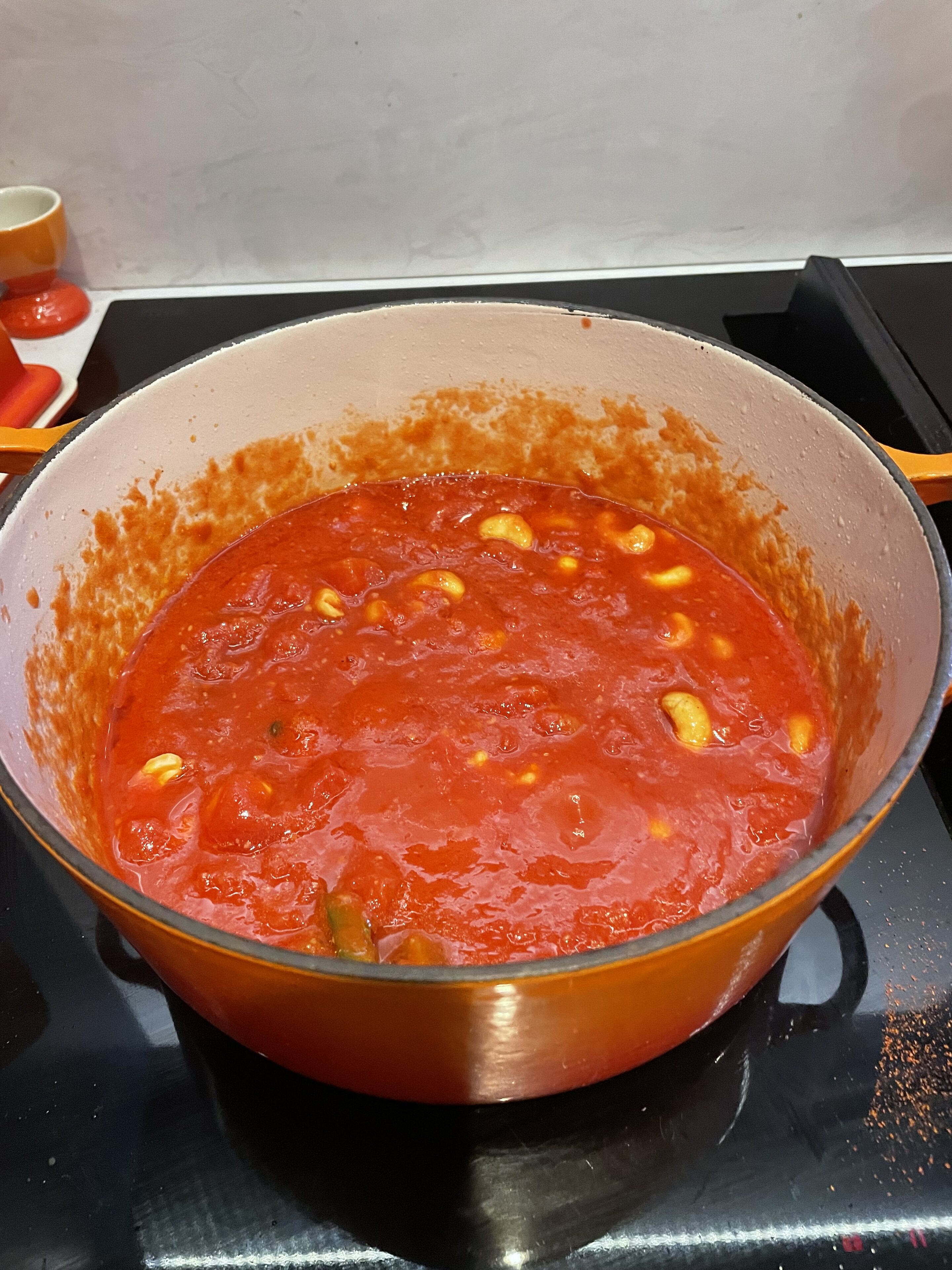 Pistonheads - The image displays a cooking scene with a focus on the preparation of a tomato-based sauce. A large pot sits on top of a stove, filled with red sauce and a few chunks of meat. The sauce is rich and red, suggesting it could be a chili or spaghetti sauce. To the right of the pot, there are fresh red bell peppers and several tomatoes. On the left side of the image, a bowl full of chopped garlic can be seen, indicating that it might be used as an ingredient in this dish. The setting appears to be a kitchen, with a white countertop and a black stove visible in the background.
