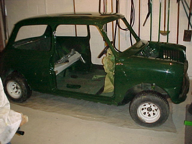 Advice Pistonheads Purchase - The image shows a vintage green car that appears to be in the process of restoration or rebuilding. The car is situated in a garage that has a concrete floor and walls. The car has its hood open, revealing the engine and its surroundings. Behind the car, several tools and other machinery are visible, suggesting a workshop environment. The car's paint is faded and chipped in places, indicating some level of wear, which is expected in the context of vintage cars and restoration projects.