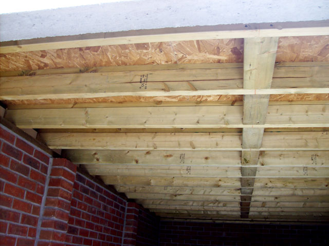 A wooden bench in front of a building - Pistonheads - The image presents a semi-enclosed space under which a wooden ceiling is under construction. The ceiling is composed of wooden studs and beams crossed with support beams, forming an intricate pattern of wood. The floor of the room appears to be made of red bricks, adding a traditional touch to the loft. The photo is taken from a low angle, providing a unique perspective on the construction work. The wooden studs are visible against the juxtaposed brick wall, indicating the ongoing structural improvements in this room.