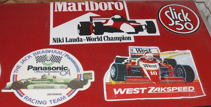 Show Us Your Stickers! - Page 1 - Formula 1 - PistonHeads - The image features a red surface with various stickers placed on top. These stickers are associated with the motorsport racing team of Marlboro, championship sponsors and ever-present in Formula 1 racing. Two predominant racing cars stand out - the "Pansonic" racing car and the iconic "West" car from a previous era. The stickers creatively feature these cars, one appearing to be in a spin or anticipating a lap. The text "MARLBORO" and "PANASONIC" are visible, further emphasizing the company's involvement in the sport.