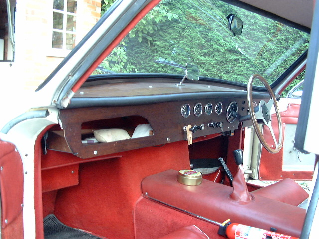 Clear picture of Grantura MK1 dashboard. - Page 1 - Classics - PistonHeads - The image displays the interior of a classic car, focusing on the dashboard area. The dashboard appears to be vintage, featuring a red material that contrasts with the green exterior of the car. There are several controls and gauges visible on the dashboard. Also present is a steering wheel on the right side of the image, indicating the vehicle's condition for driving. The overall style of the image suggests it could have been taken to depict the classic car's interior layout. The vehicle shows signs of age and use, adding to its antique appeal.